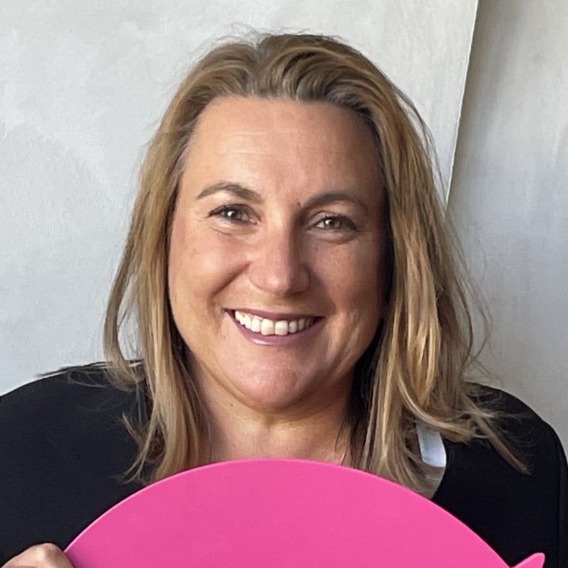 Woman in a black suit, holding a large DonateLife heart, smiling at the camera.